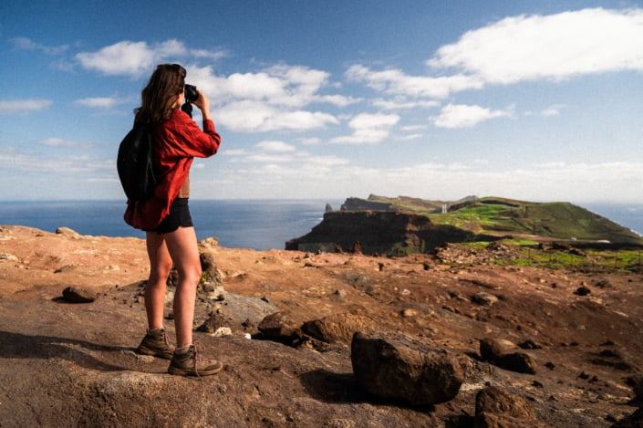 A girl in a red shirt looking at the cliffs of Madeira island's Eastern tip through binoculars