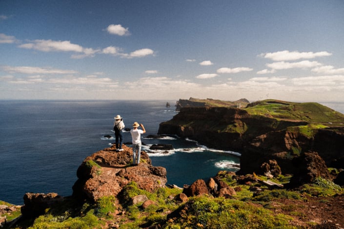 A digital nomad couple standing on a cliff admiring the beautiful coastal landscape of Madeira island and taking pictures