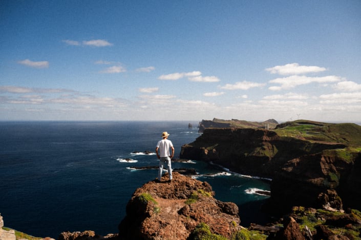 A lonesome male nomad in a white shirt on a rock by the sea, looking into distance, landscape format