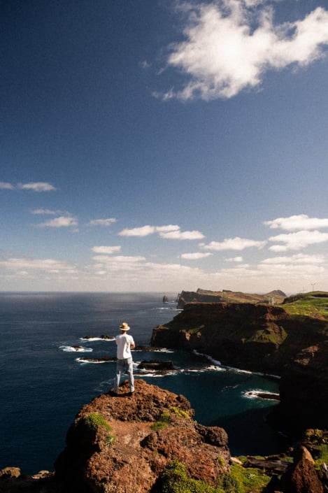 A lonesome male nomad in a white shirt on a rock by the sea, looking into distance