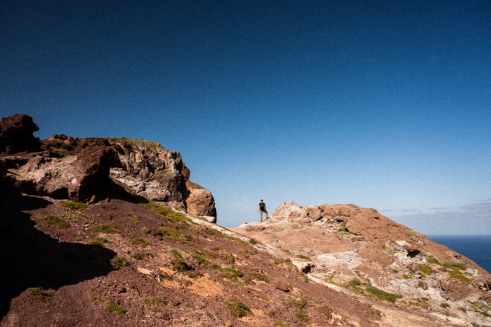 Christoph with binoculars in a rocky desert landscape, blue sky and ocean in the background