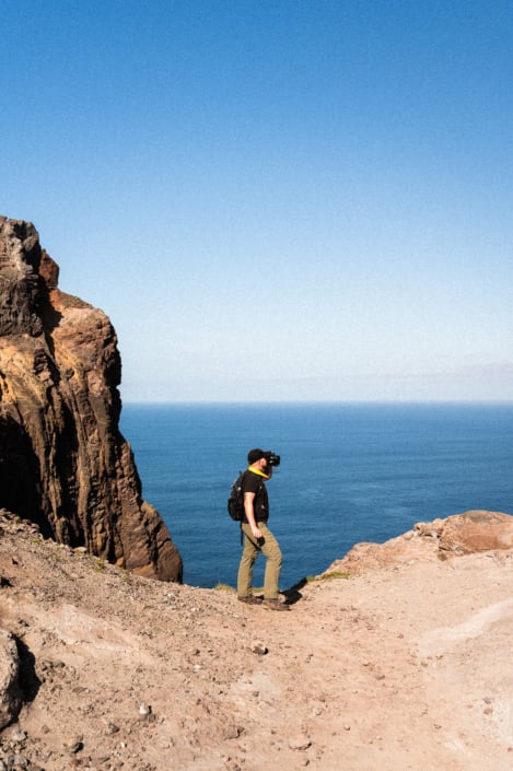 Christoph with binoculars at a cliff, blue sky and ocean in the background