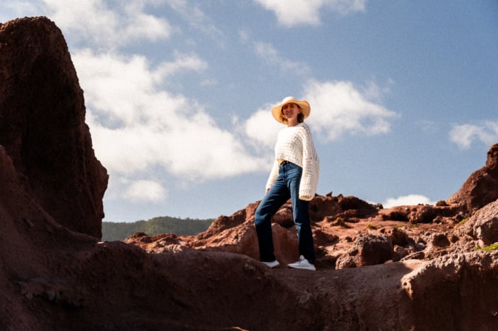 A girl in white shirt with hat standing on rocks with blue sky in the background