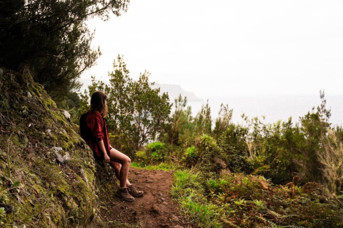 A girl in a red shirt resting aside a hiking trail