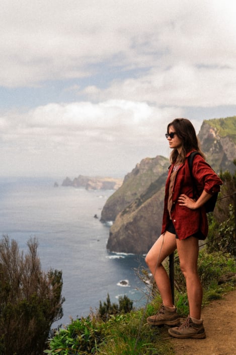 Girl in sunglasses and a red shirt standing on a cliff by the sea