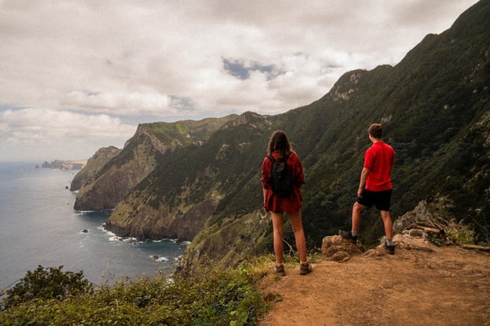 A couple, both in red shirts, standing on a cliff looking at the northern coast of Madeira island