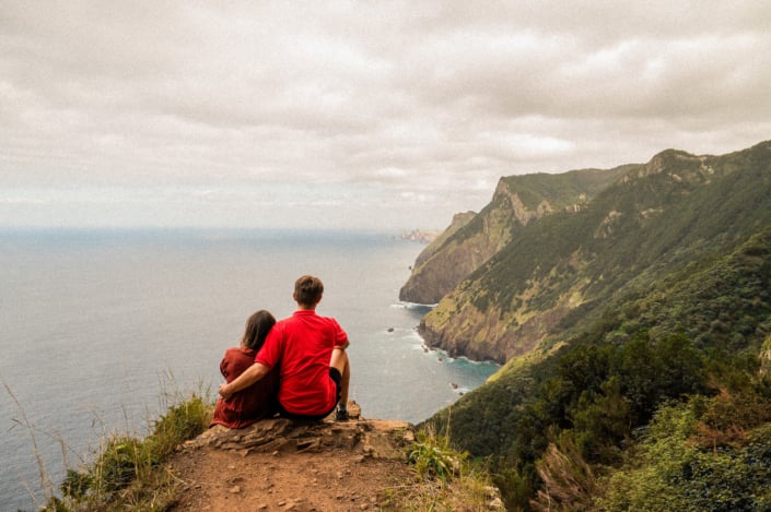 Couple in red shirts sitting on a cliff at the coast line of Madeira island, landscape format